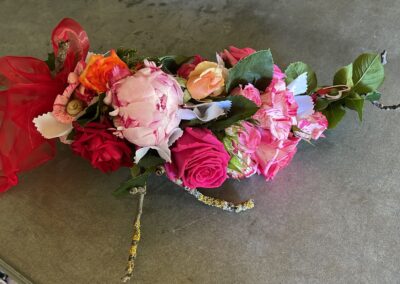 Tischdekoration, bestehend aus unterschiedlichen Rosen und anderen Blumen, Pflanzen und Bändern.