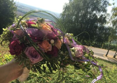 Fertiger Blumenstrauß mit unterschiedlichen Rosen, Bändern und Blättern.