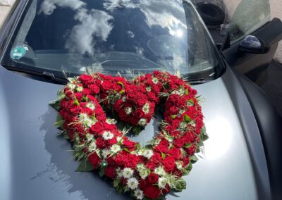 Herzförmiges, rotes Rosengesteck auf einem grauen Audi.