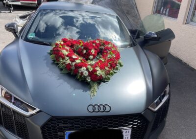 Herzförmiges, rotes Rosengesteck auf einem grauen Audi.