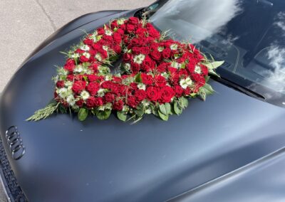 Herzförmiges, rotes Rosengesteck auf einem grauen Audi.